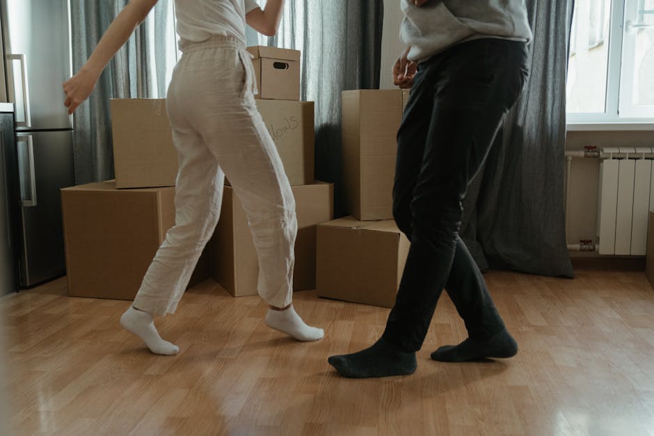 A professional removal worker from Removal Company Enfield is inside a bright, spacious room during a home relocation process, carrying two large cardboard boxes stacked on top of each other. The work